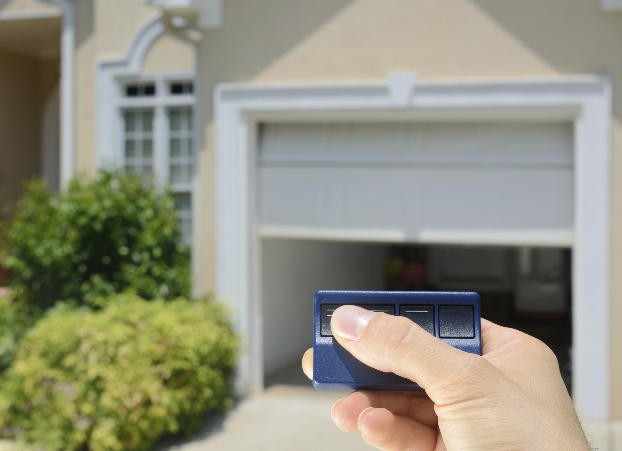 hand holding a blue garage door opener remote opening a garage door